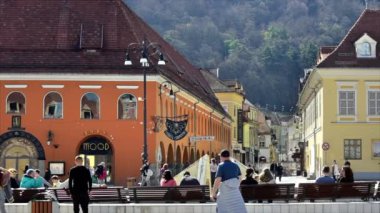 BRASOV, ROMANIA - Nisan 2022: Eski şehir merkezindeki Konsey Meydanı manzarası. Klasik binalar, bir sürü yürüyen ve dinlenen insan.
