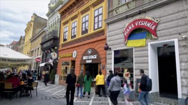BRASOV, ROMANIA - Nisan 2022: Eski şehir merkezi manzarası. Bir sürü yürüyen insan, restoran ve eski binalarla dolu bir yaya sokağı.