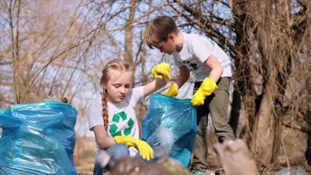 男孩和女孩在一个被污染的地方的袋子里收集塑料垃圾 回收T恤衫上的标识 慢动作 — 图库视频影像