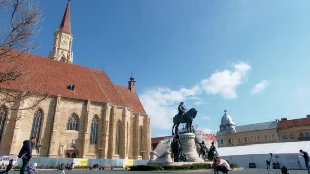 Cluj Romania エイプリル 2022 市街地の街並み 聖ミカエル教会とその前にマティアス コルヴィヌスの像を持つ中央広場 人々を歩く — ストック動画