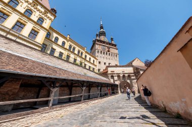 SIGHISOARA, ROMANIA - Mayıs 2022: Kasaba Tarihi Merkezi manzarası. Önünde insanlar olan saat kulesi, eski binalarla dar sokaklar.