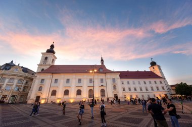 SIBIU, ROMANIA - 2022 MAYIS: günbatımında kasabanın tarihi merkezinin görüntüsü. Büyük Meydan 'da birçok insan ve klasik tarzda yapılmış eski binalar var.