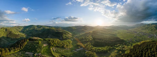 Aerial drone view of nature in Maramures, Romania. Carpathian mountains, town located in a valley with hills covered with lush forest around it, river, sunset
