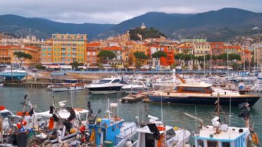 Akdeniz limanında birden fazla demirli yat ve tekne var. Sanremo, İtalya 'da arka planda klasik binalar. Bulutlu gökyüzü