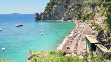 POSITANO, İTALYA - Mayıs 2022: Tyrhenian deniz kıyıları manzarası. Tekneler, insanlarla dolu sahil, uzakta kale, yeşillik.