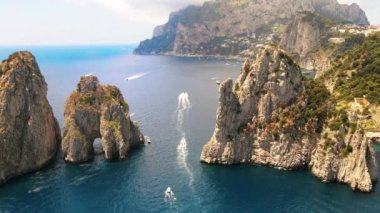 İtalya, Capri 'deki Tyrhenian deniz kıyılarının insansız hava aracı görüntüsü. Kayalık kayalıklar, mavi su, yüzen kayıklar, yeşillik, uzaktaki kasaba