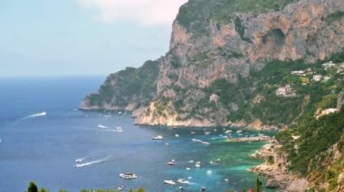 İtalya, Capri 'nin Tyrhenian deniz kıyıları. Kayalık kayalıklar, mavi su, birden fazla yüzen tekne, yeşillik