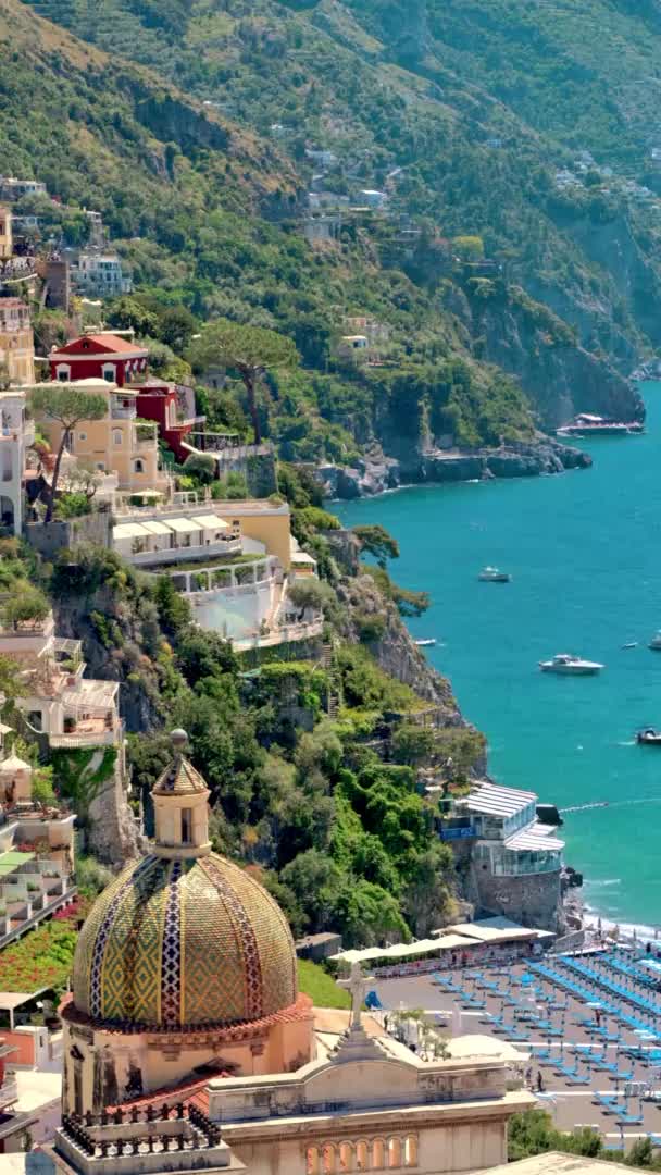 Street scape of Positano, který se nachází na pobřeží Tyrhénského moře, Itálie. Řady obytných budov, útesy, zeleň, lodě v dálce. Svislé zobrazení