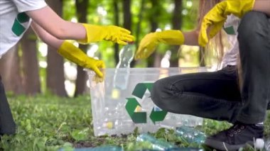 Erkek ve kız, kirli bir parktaki konteynırda plastik çöp topluyor tişörtlerdeki geri dönüşüm işaretlerini topluyor. Yavaş çekim