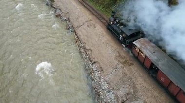 VİSEU DE SUS, ROMANIA - MAYIS, 2022: Mocanita 'nın içinde işçiler, yemyeşil orman ve nehir bulunan bir vadide hareket halindeki buhar treni görüntüsü