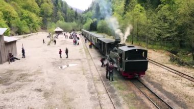 VISEU DE SUS, ROMANIA - MAYIS, 2022: Mocanita buharlı treninin demiryolu istasyonundaki bir vadideki hava aracı görüntüsü, dinlenen turistler, yemyeşil orman ve nehir çevresi