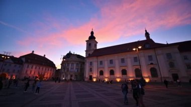 SIBIU, ROMANIA - 2022 MAYIS: günbatımında kasabanın tarihi merkezinin görüntüsü. Büyük Meydan 'da birçok insan ve klasik tarzda yapılmış eski binalar var.