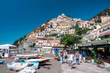 POSITANO, ITALY - JUNE, 2022: View of the town located on the Tyrrhenian sea coast. Rows of residential buildings located on hill slope, beach with people, greenery