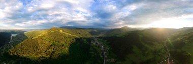 Aerial drone panoramic view of nature in the Carpathians in Romania at sunset. Village located in a valley, hills covered with lush forest