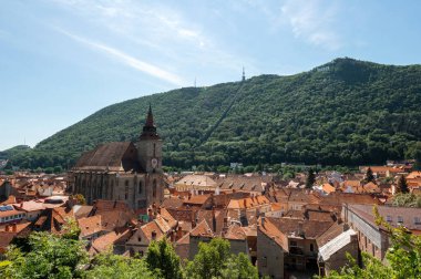 Romanya 'nın eski Brasov merkezindeki Kara Kilise' nin insansız hava aracı görüntüsü. Çevresindeki eski binalar, yeşillikli tepeler.