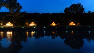 Gölün önündeki aydınlık çadırlar. Glamping 'de. Orman, gece.