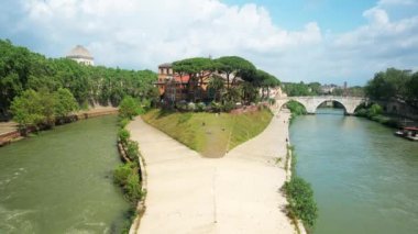 View of The Tiber Island in Rome, Italy. Island surrounded by Tiber river with resting people, old buildings and greenery