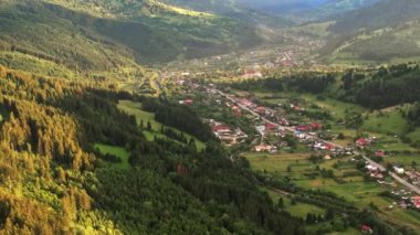 Günbatımında Romanya 'daki Karpatlar' da doğanın insansız hava aracı görüntüsü. Vadideki köy, yemyeşil ormanlarla kaplı tepeler.