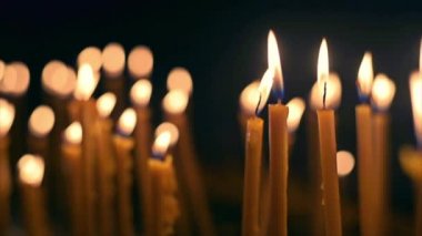 Close view of lots of burning candles with black background. Slow motion