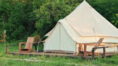 Tent with wooden chairs in front of it at glamping, lush forest around