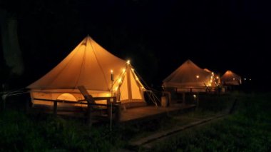 Glamping 'de yanan meşaleleri, lambaları ve tahta sandalyeleri olan çadırlar.