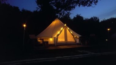 Tents with burning torches, lamps and wooden chairs at glamping, night