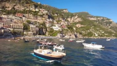 POSITANO, İtalya - Haziran 2022: Tyrhenian deniz kıyısı manzarası. Klasik binalar, yüzen tekneler, yeşillik. Bir gemiden görünüm