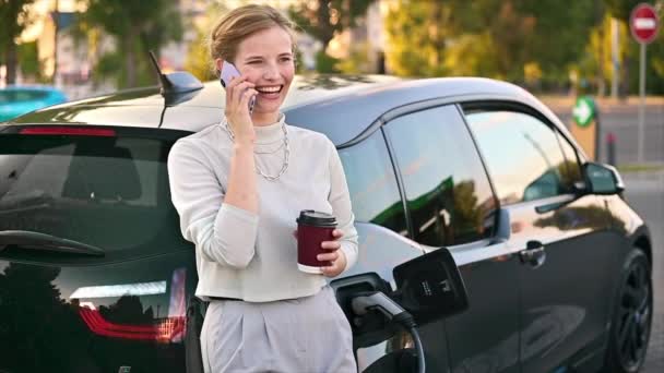 Young Blonde Woman Coffee Talking Smartphone Car Charging Station Electric — Vídeos de Stock