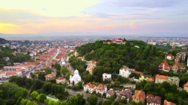 Aerial drone view of The Citadel in Brasov at sunset, Romania. Medieval fortress on the top of a hill. Buildings and green trees around