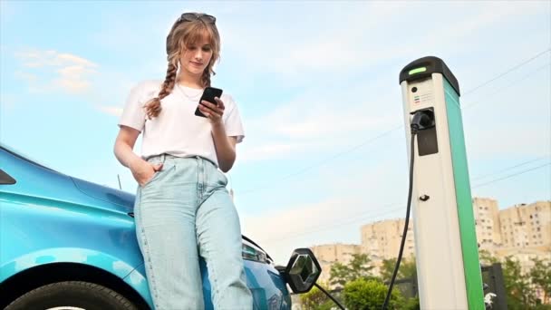 Young Blonde Woman Using Smartphone Car Charging Station Charging Electric — Vídeo de stock
