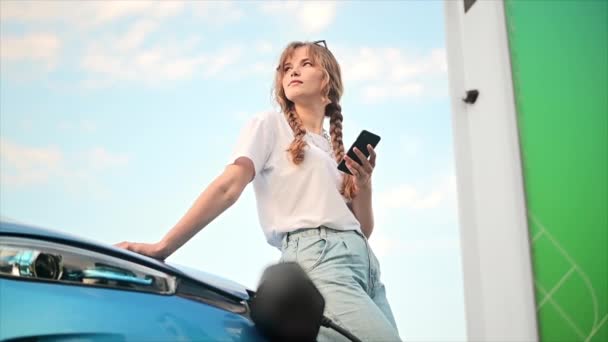 Молодая Блондинка Использующая Смартфон Зарядной Станции Автомобиля Зарядкой Электромобиля Отрицательное — стоковое видео