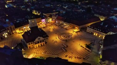 Aerial drone view of main central square in Brasov at night, Romania. Old city centre with County Museum of History, Black church, buildings, nightlights, people