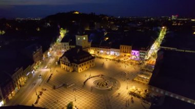 Aerial drone view of main central square in Brasov at night, Romania. Old city centre with County Museum of History, Black church, buildings, nightlights, people
