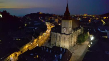 Aerial drone view of main central square in Brasov at night, Romania. Old city centre with County Museum of History, Black church, buildings, nightlights, people
