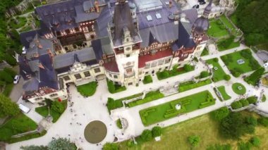 Aerial drone view of The Peles Castle in Romania. Castle with gardens and tourists in Carpathians, lush forest around it