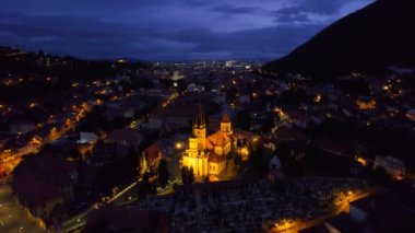Aerial drone view of the Saint Nicholas Church in Brasov at night, Romania. Medieval church with multiple buildings and roads with nightlights
