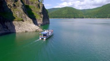 View of nature in Romania. Valley in Carpathian mountains with Vidraru lake, floating boat with people, green slopes around