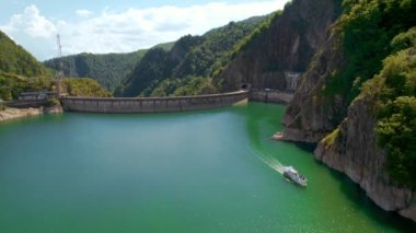 View of nature in Romania. Valley in Carpathian mountains with Vidraru dam and lake, floating boat with people, green slopes around