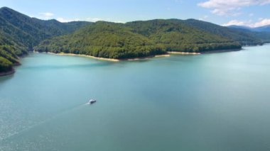 View of nature in Romania. Valley in Carpathian mountains with Vidraru lake, floating boat with people, green slopes around