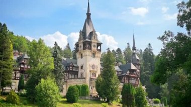 View of The Peles Castle in Romania. Castle with gardens and tourists in Carpathians, lush forest around it