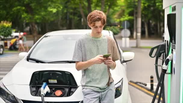 Young Man Using Smartphone Car Charging Station Charging Electric Car — Vídeos de Stock