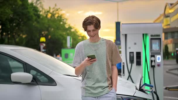 Young Man Using Smartphone Car Charging Station Charging Electric Car — Vídeo de stock