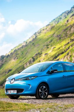 TRANSFAGARAS, ROMANIA - JULY, 2022: Parked electric Renault ZOE at Transfagarasan route. Mountains slopes covered with greenery on the background. Vertical view