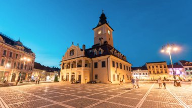 BRASOV, ROMANIA - JULY, 2022: View of the old city centre at evening. Council Square with County Museum of History and people, restaurants, old buildings, moving cars