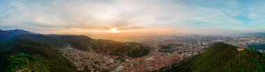 Aerial drone panoramic view of Brasov at sunset, Romania. Old city centre with buildings, hills and greenery
