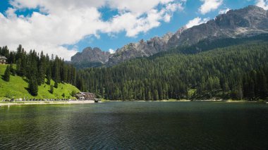 Dolomite Alps in Italy. View of a lake with forest, buildings and parked cars around, mountains on the background