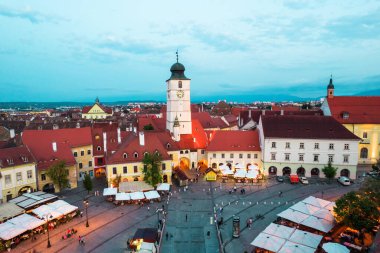 Aerial drone view of the Historic Centre of Sibiu at evening, Romania. The Great Square with old buildings around, narrow streets, people, illumination