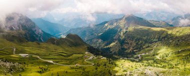 Dolomite Alps in Italy. Panoramic view of mountains and slopes covered with greenery and forest, low clouds, road with cars
