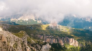 Dolomite Alps in Italy. View of mountains and slopes covered with greenery and forest, low clouds, road with cars