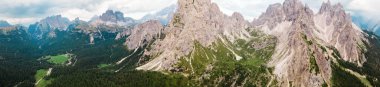 Dolomite Alps in Italy. Panoramic view of mountains and slopes covered with greenery and forest, low clouds